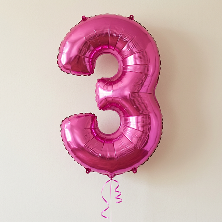 Pink number 3 balloon floating with bright pink curling ribbon against a softly lit neutral wall, in square format