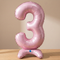Pink number 3 balloon on a wooden table with a neutral background and soft light and shade, square format