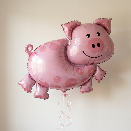 Pink pig balloon floating with pink curling ribbon against a neutral wall with soft light and shade, close up in square format