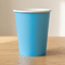 Plain blue paper cup on a wood table with a neutral background and soft light and shade, square format