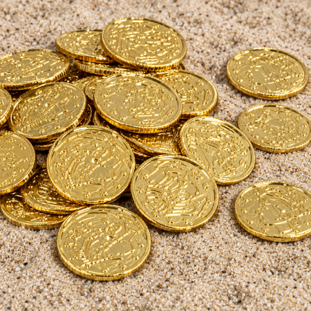 Plastic gold coins close up on sand, in square format
