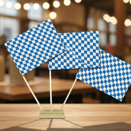 Three small blue-and-white checkered flags on wooden sticks, displayed on a tabletop with a softly blurred indoor background.