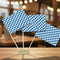 Three small blue-and-white checkered flags on wooden sticks, displayed on a tabletop with a softly blurred indoor background.