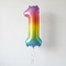Rainbow number one balloon floating with silver curling ribbon against a white wall with soft light and shade
