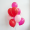 Realistic red and pink balloon bouquet against a white wall with soft light and shade, in square format