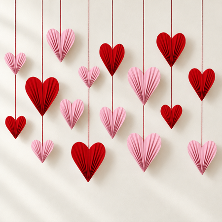 Red and pink paper hearts against an off-white wall with soft light and shade, with strings extending beyond the top of the square image