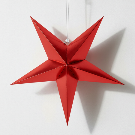 Red foil paper star against a white wall with light and shade