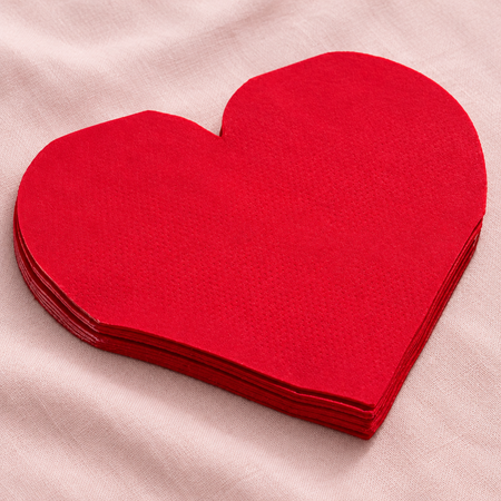 Red heart-shaped paper napkins close up on a pale pink tablecloth with soft light and shade, in square format