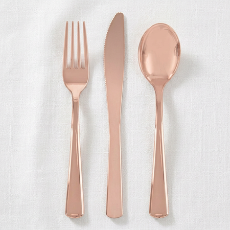 Rose-gold cutlery viewed from above on a white tablecloth with soft light and shade, close up in square format