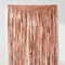 Rose gold foil curtain close up against a white wall with natural light and shade, in square format