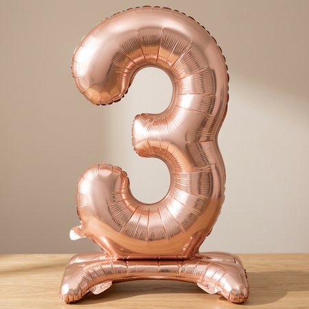 Rose gold number 3 balloon on a wooden table with a neutral background and soft light and shade, square format