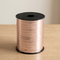 Rose-gold ribbon spool close up on a wooden table with a neutral background, in square format