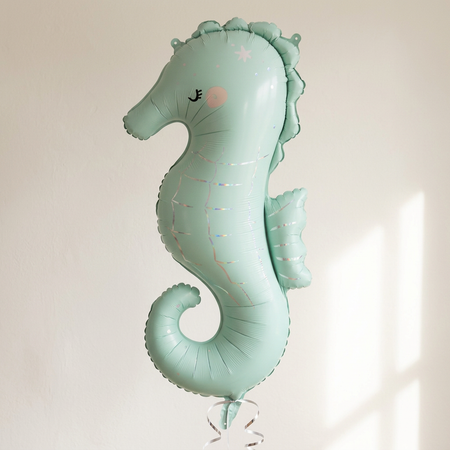 Seahorse balloon floating with silver curling ribbon against a neutral wall, in square format