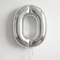 Silver number 0 balloon with silver curling ribbon against a softly lit white wall