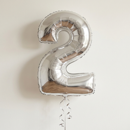 Silver number 2 balloon floating with matching silver curling ribbon against a neutral background with soft light and shade