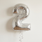 Silver number 2 balloon floating with matching silver curling ribbon against a neutral background with soft light and shade