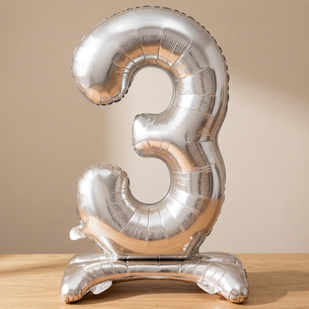 Silver number 3 balloon on a wooden table with a neutral background and soft light and shade, square format