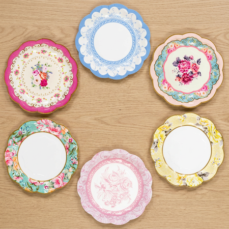Six floral paper plates on a natural wood background, viewed from above in square format