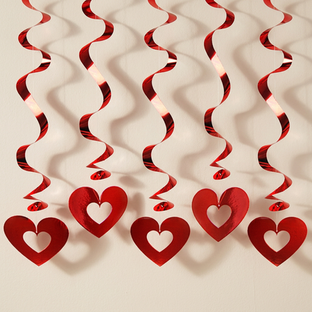 Square close-up of five red hanging swirl hearts against an off-white wall with soft light and shade