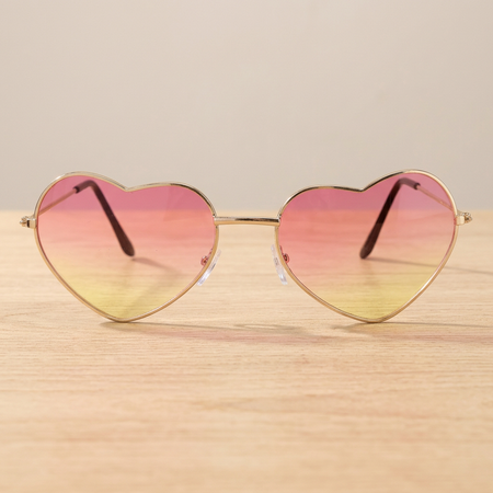 Square close-up of the pink and yellow heart-shaped glasses on a wooden table with a neutral background