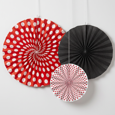 Square close-up of the three paper fans against a white wall, with soft light and shade and strings extending off the top edge