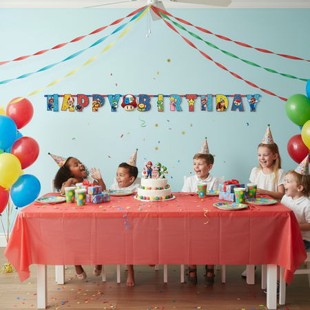 Children celebrating a birthday with a cake and decorations in a room with a 'Happy Birthday' banner.
