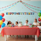 Children celebrating a birthday with a cake and decorations in a room with a 'Happy Birthday' banner.
