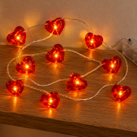 Ten red wire heart lights glowing close up on a wooden shelf, in square format