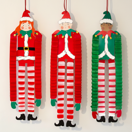 Three hanging paper elf decorations against a warm off-white wall