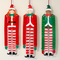 Three hanging paper elf decorations against a warm off-white wall