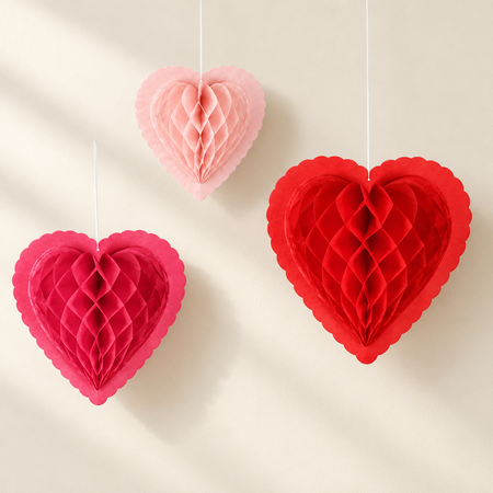 Three honeycomb hanging hearts against a cream wall with soft light and shade