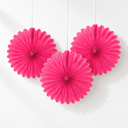 Three pink paper fans against a white wall with soft light and shade