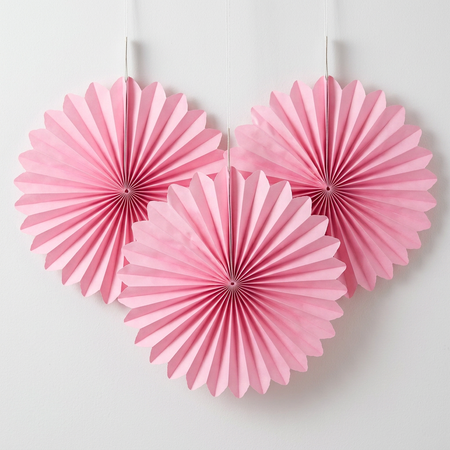 Three pink paper fans really close up against a white wall with soft light and shade, in square format