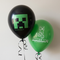 Two Minecraft balloons floating against a softly lit neutral wall with black curling ribbons, close up in square format