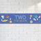 Two the Moon banner on a white brick wall with natural light and shade, in square format