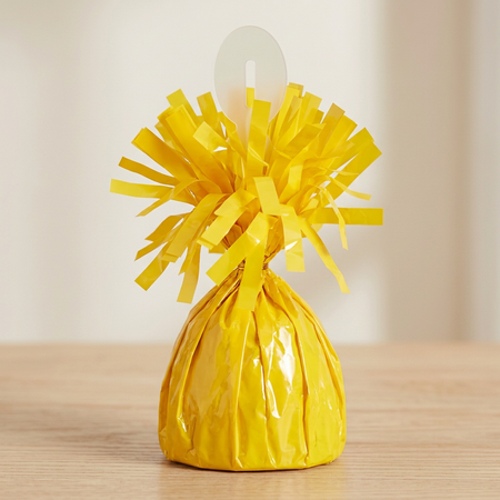 Yellow balloon weight close up on the matching wooden table with a neutral background and soft lighting, in square format