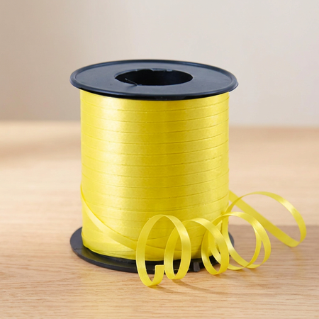 Yellow curling ribbon reel on the matching wooden tabletop with a neutral background and soft lighting, in square format